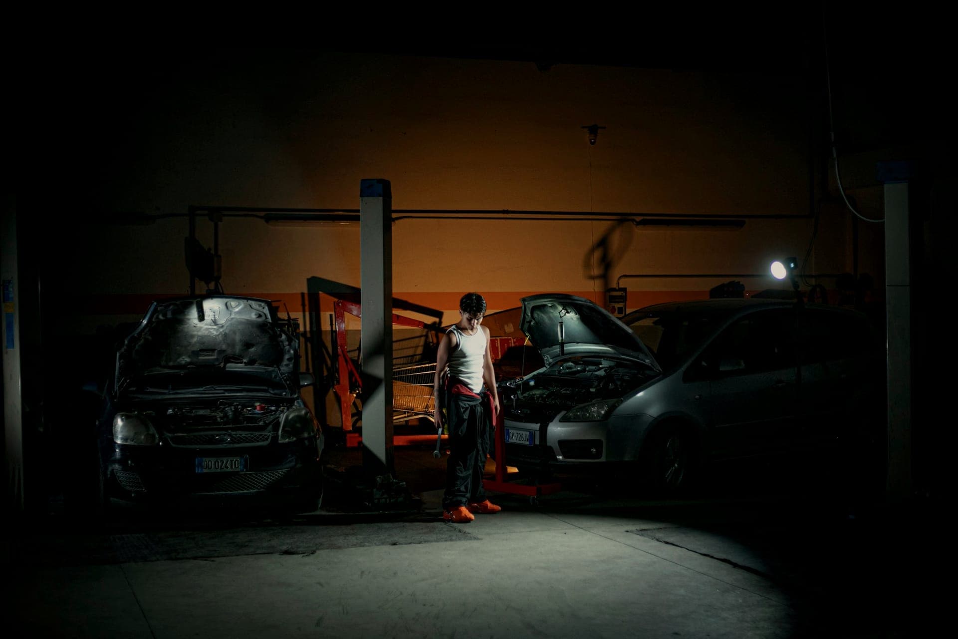 Mechanic between cars on lifts in a dimly lit workshop